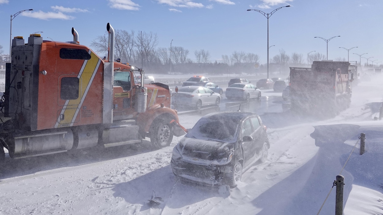 Des camions et une voiture endommagée sur le bord d'une route enneigée.