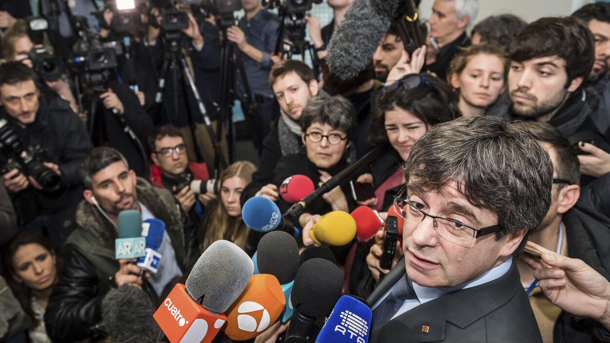 Carles Puigdemont tourne la tête vers l'objectif d'une caméra. Devant lui, des dizaines de journalistes.