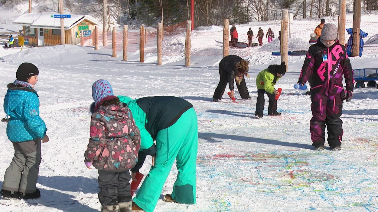 Des enfants en habits de neige dessinent sur la neige avec des jets de couleurs.