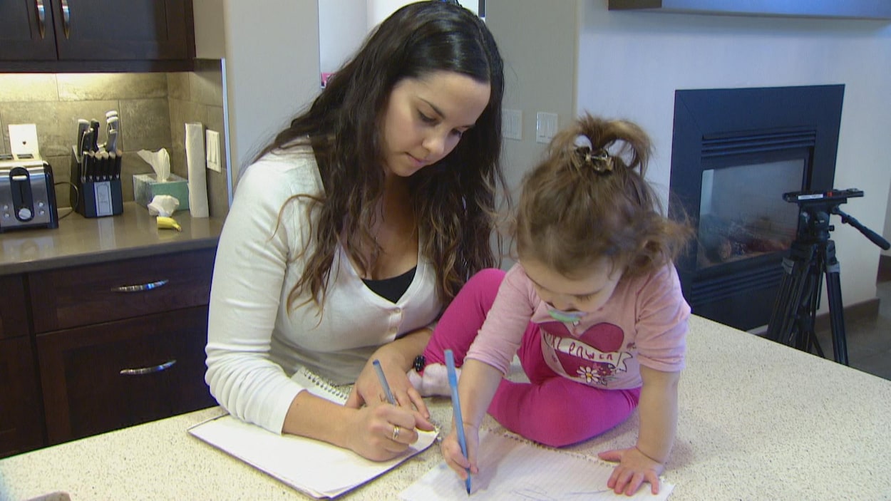 Une jeune femme et une petite fille écrivent chacune sur une feuille de papier, dans une cuisine.