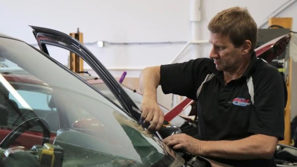 Un homme installe un pare-brise sur une auto.