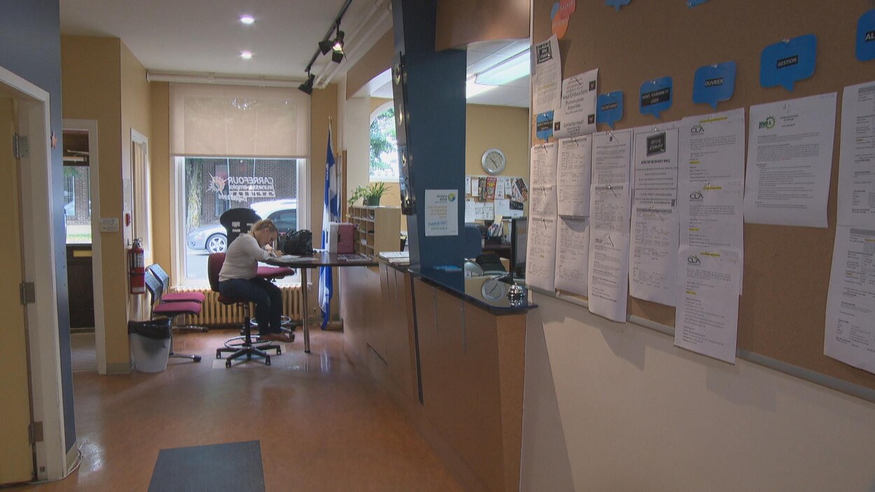 Une jeune femme rempli un formulaire. Un mur rempli d'offre d'emploi à droite.