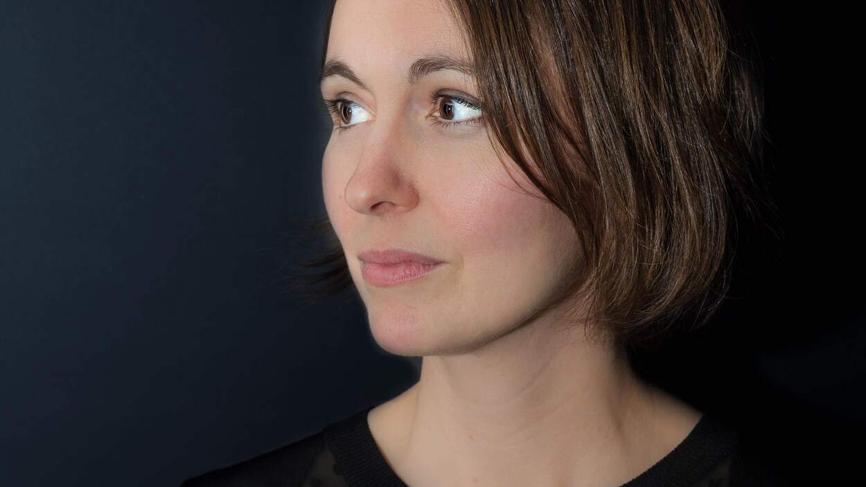 Portrait en couleur sur fond noir. La jeune femme ne regarde pas l'objectif, elle a le visage tourné de trois-quarts vers la droite. Elle porte un haut noir et des cheveux châtains au carré lâchés.