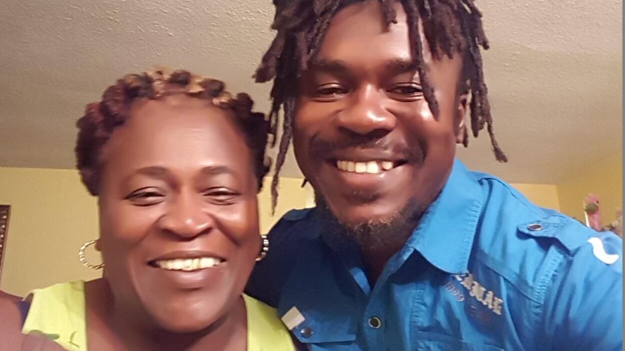 Une femme et un homme noirs sourient devant une caméra.