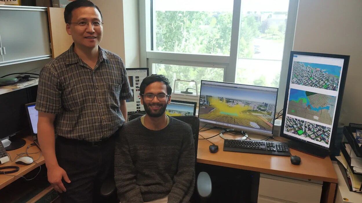 Deux hommes posent devant des écrans d'ordinateur placés sur un bureau.