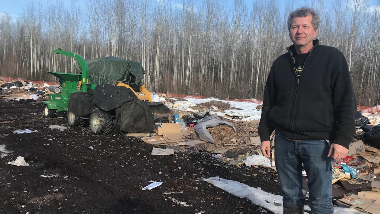 Un homme se tient debout dans un dépotoir, devant un secteur boisé.