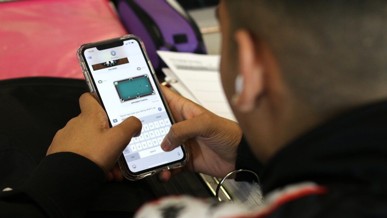 Un élève regarde l'écran de son téléphone cellulaire, sur lequel apparaît l'image d'une table de billard.