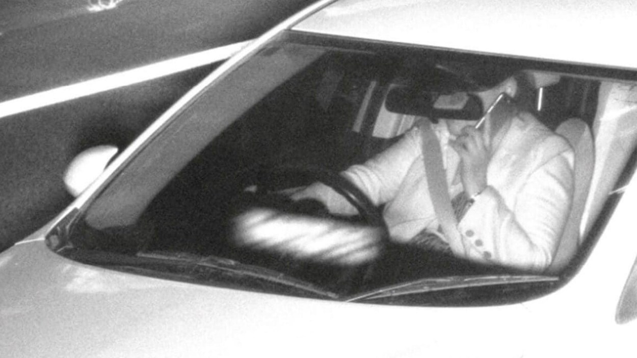 Un homme sur son téléphone cellulaire au volant d'une voiture, filmé par une caméra de surveillance.