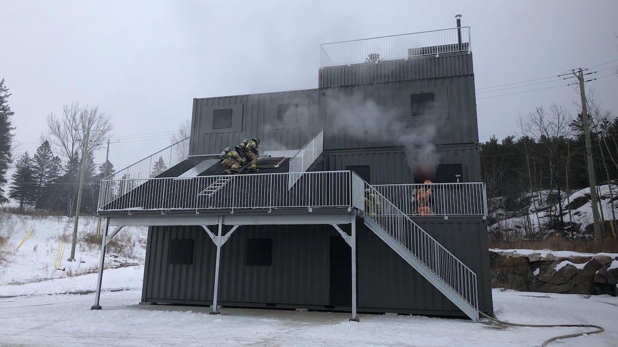 Un module d'entraînement fabriqué à partir de conteneurs maritimes autour duquel s'affairent des pompiers.