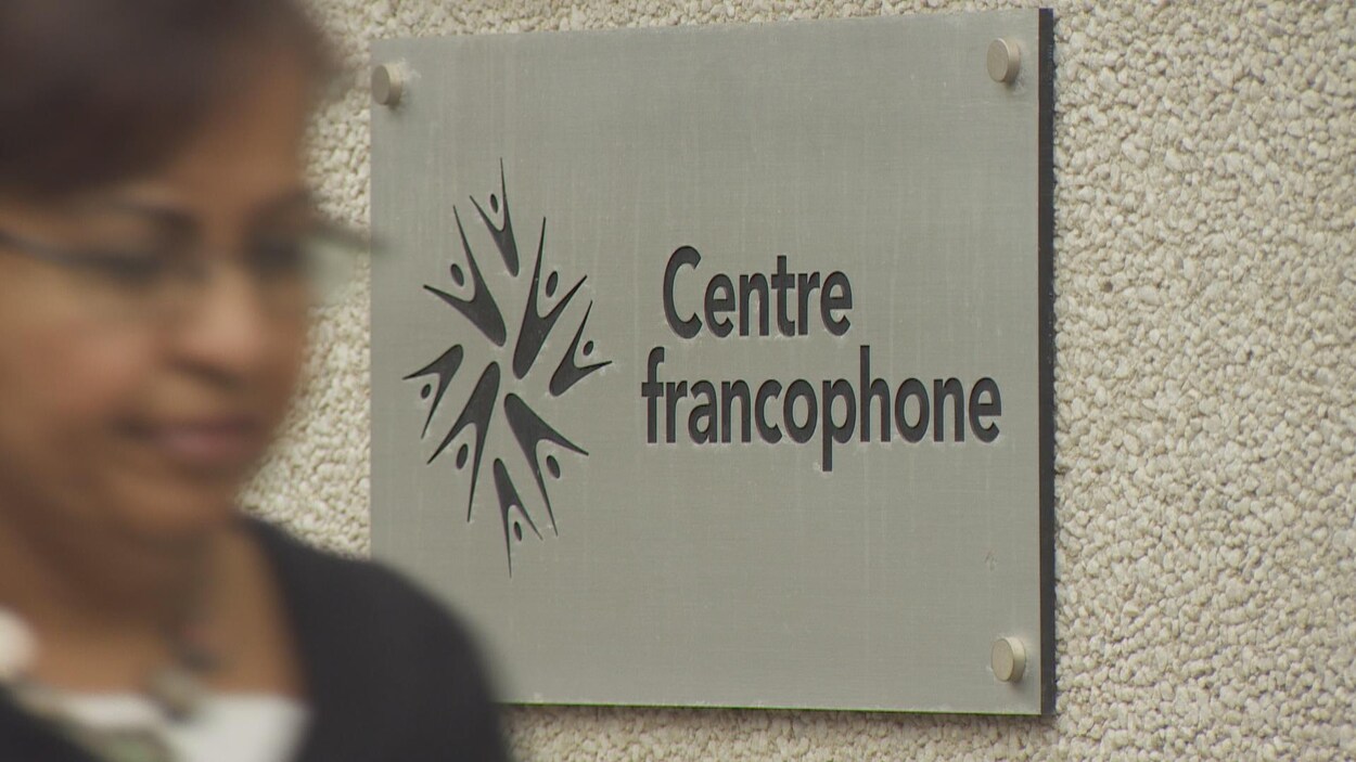 Photo d'une femme qui passe devant le panneau d'entrée du Centre francophone de Toronto.