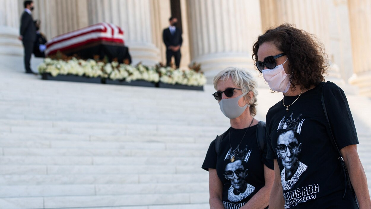 Deux femmes portant des t-shirts aux couleurs de Ruth Bader Ginsburg marchent près du cercueil de la juge, devant la Cour suprême des États-Unis.