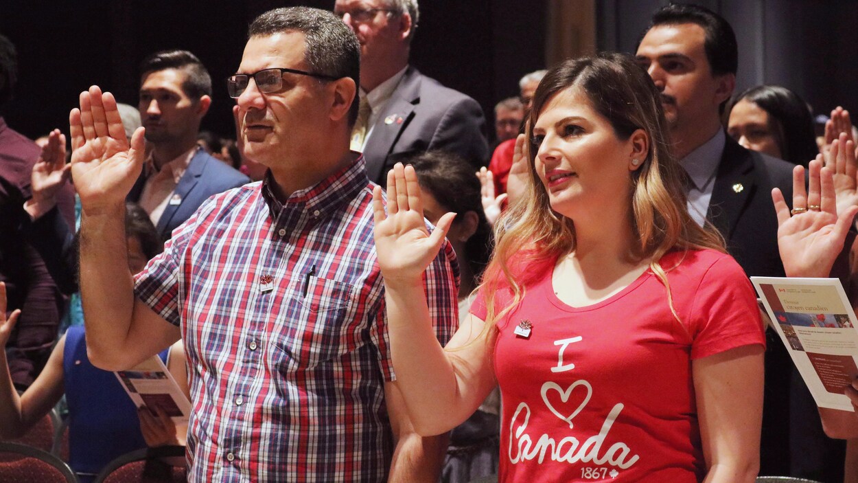 Hommes et femmes la main droite levée lors d'une cérémonie de citoyenneté canadienne.