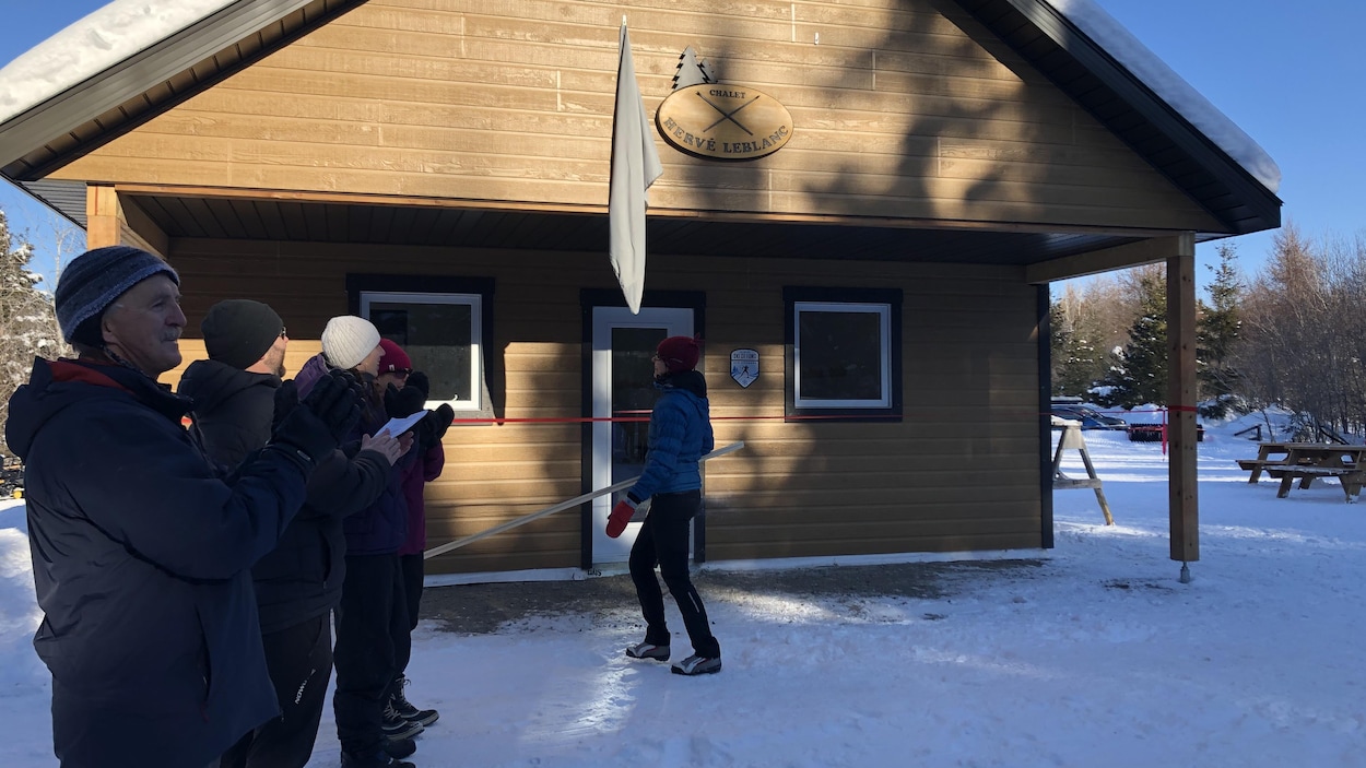 Des gens debout dehors dans la neige, devant un chalet