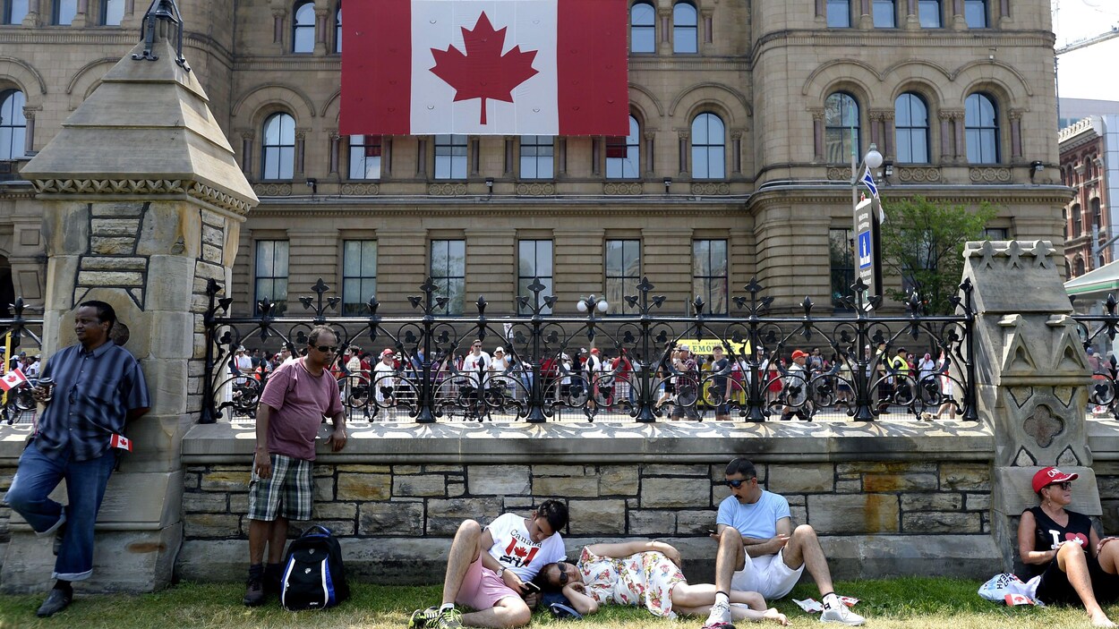 Des gens assis, couchés ou accoudés sur un muret de pierre, devant un drapeau du Canada.