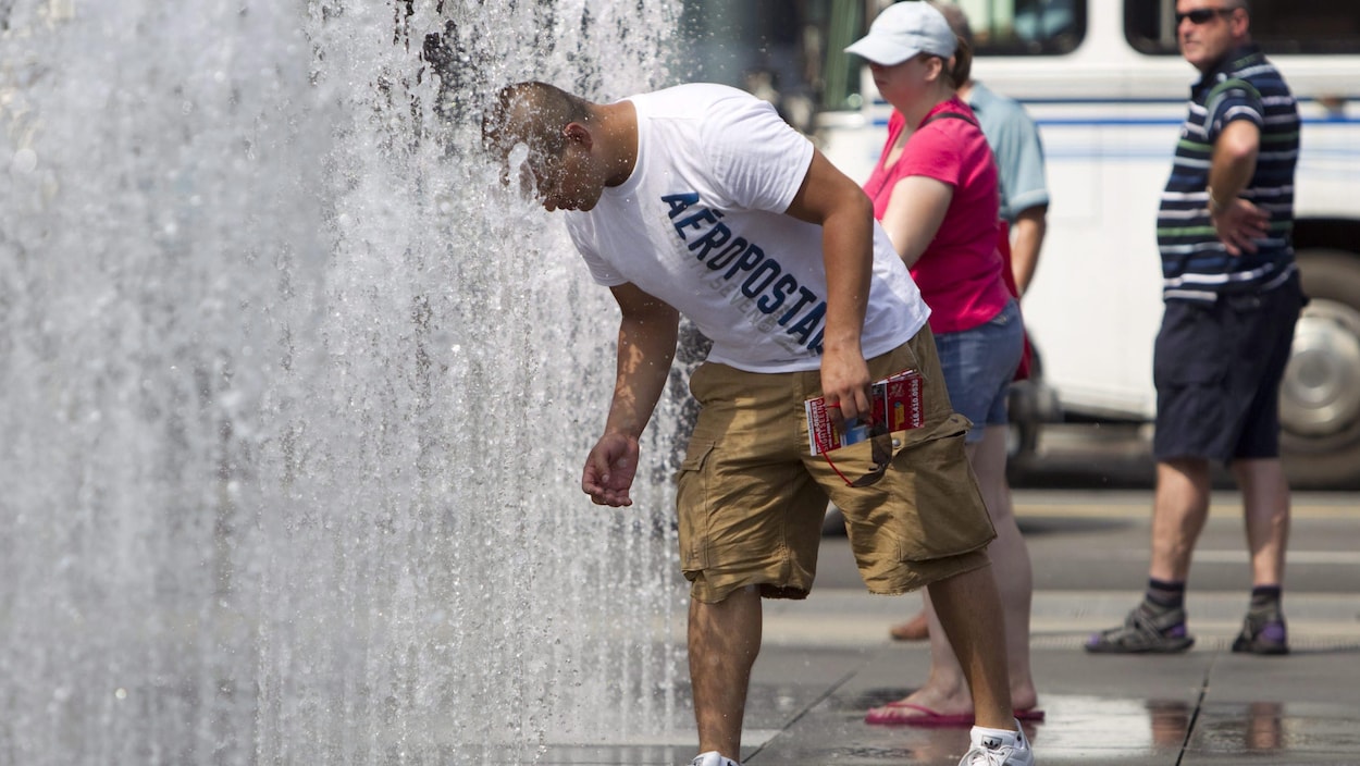Un homme se met la tête dans l'eau d'une fontaine pour se rafraîchir.