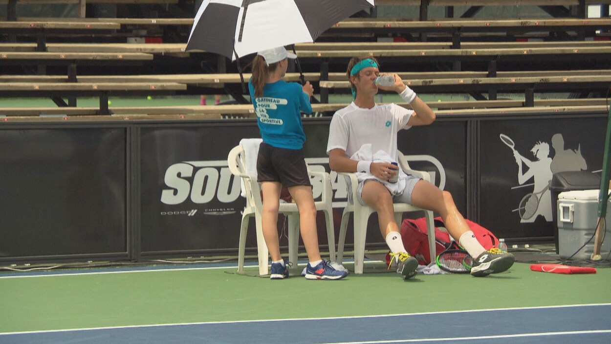 Un joueur de tennis assis boit une bouteille d'eau.