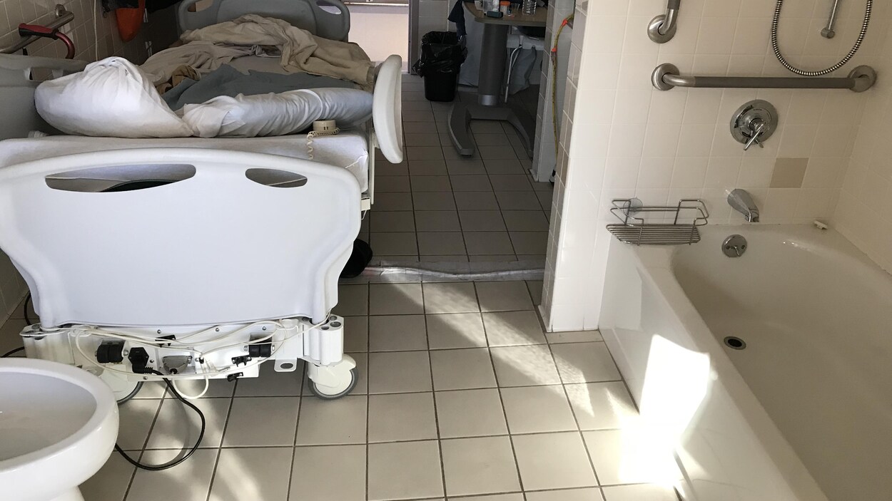 Une salle de bain transformée en chambre d'hôpital. On voit un lit d'hôpital et, au pied du lit, une toilette, et un bain à droite. Une salle de bain transformée en chambre d'hôpital. On voit un lit d'hôpital et, au pied du lit, une toilette, et un bain à droite.