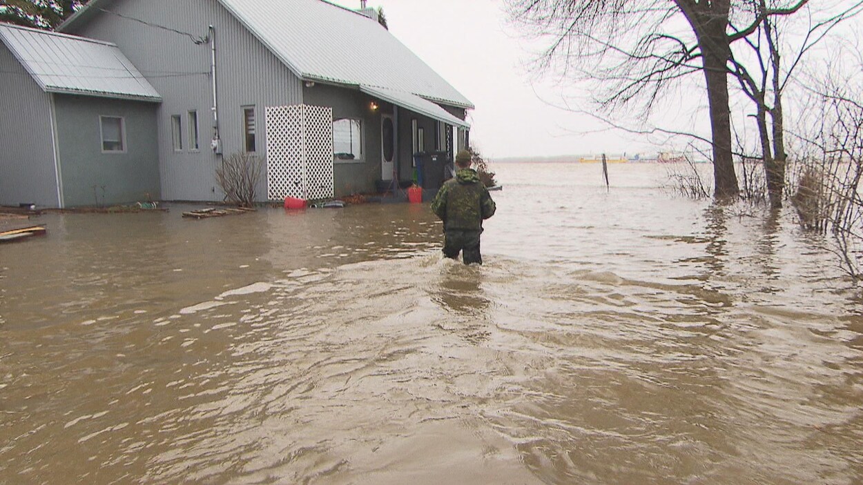 Militaire qui va vers une maison avec de l'eau jusqu'aux cuisses.