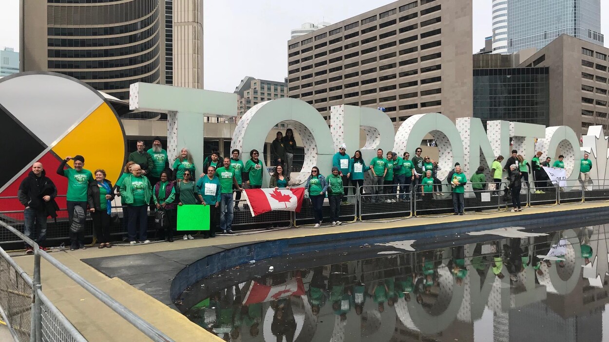 Des personnes portant des vêtements verts posent devant l'hôtel de Ville de Toronto.