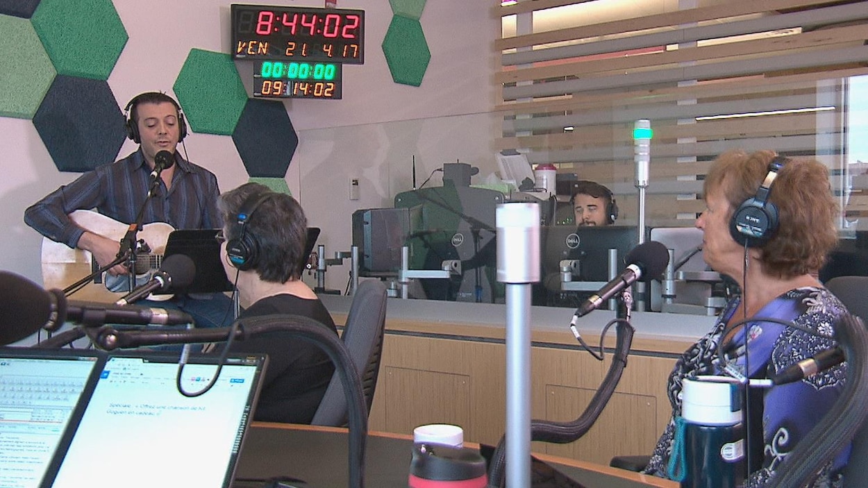 Un chanteur dans un studio de radio devant deux femmes qui l'écoutent Un chanteur dans un studio de radio devant deux femmes qui l'écoutent