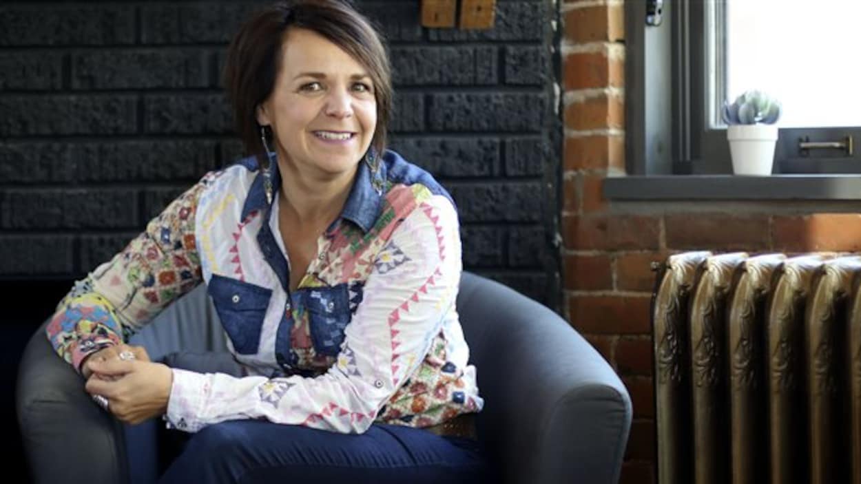 Une femme vêtue d'une chemise à motifs multicolores est assise les mains jointes dans un fauteuil bleu. Une femme vêtue d'une chemise à motifs multicolores est assise les mains jointes dans un fauteuil bleu.