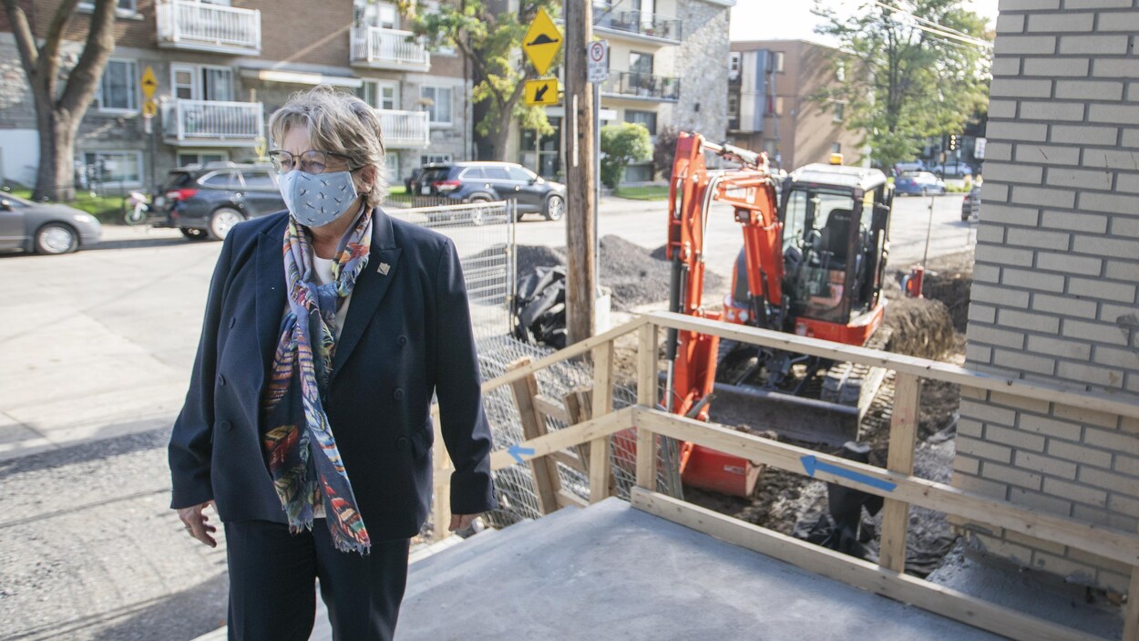 Chantal Rouleau, portant un masque, dehors à l'entrée d'une école avec, derrière elle, une tractopelle.