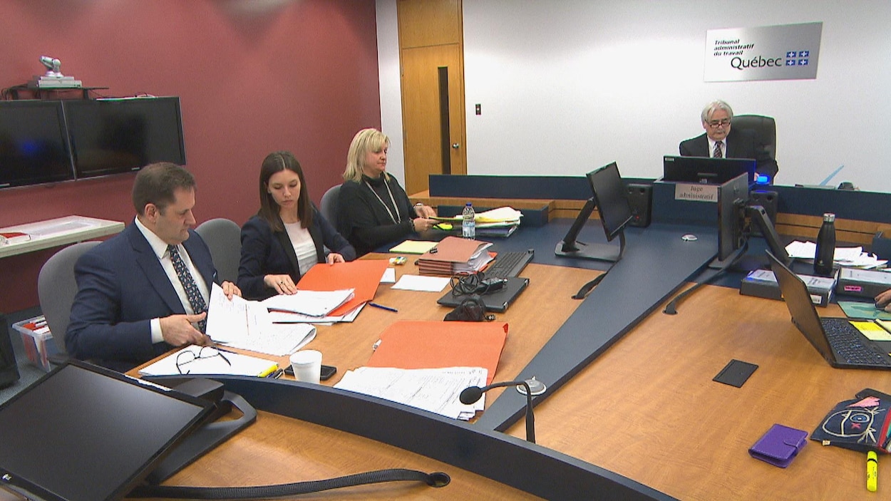 Trois personnes sont assises à gauche à une table. Un juge administratif siège au fond de la salle.