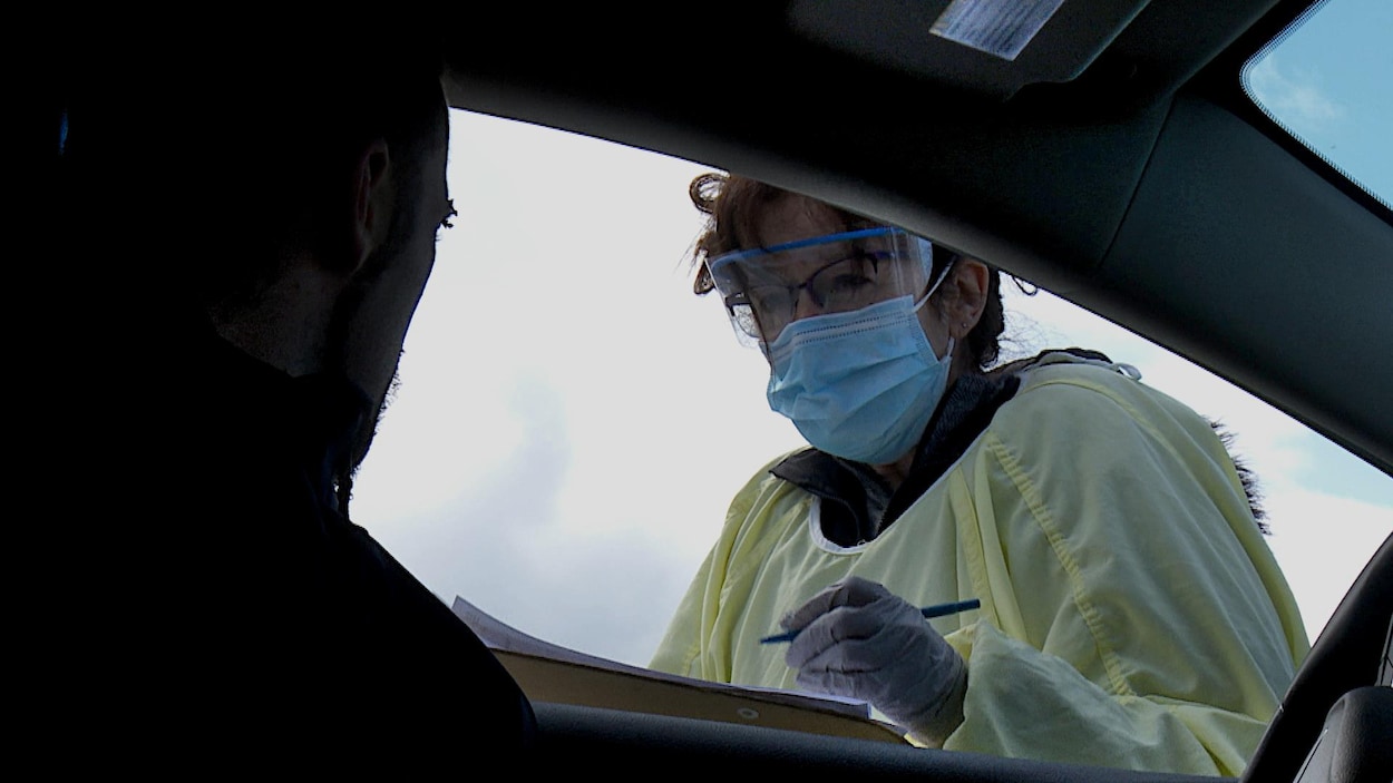 Vêtue d'équipement de protection, l'infirmière pose des questions à un automobiliste.