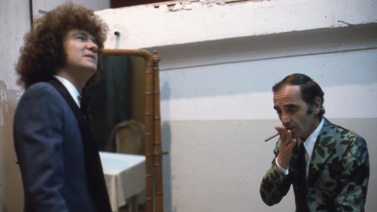 Robert Charlebois regarde en l'air et Charles Aznavour fume une cigarette.