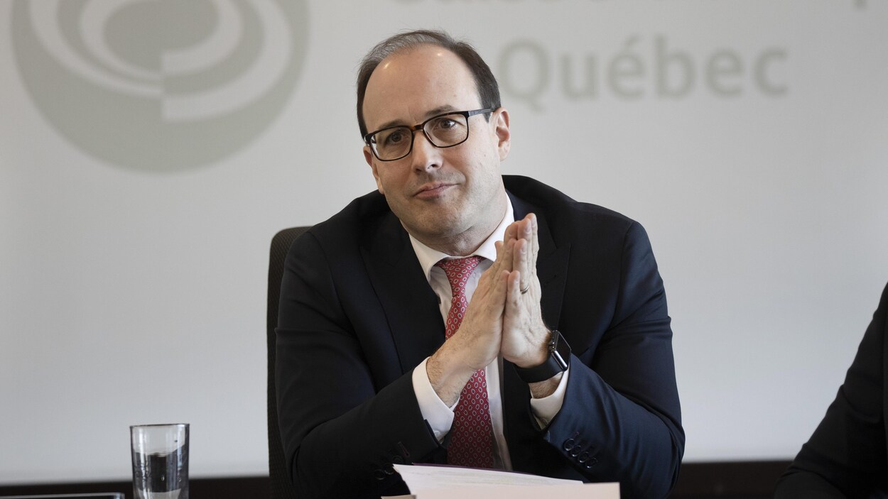 Un homme assis derrière un bureau, les mains jointes.