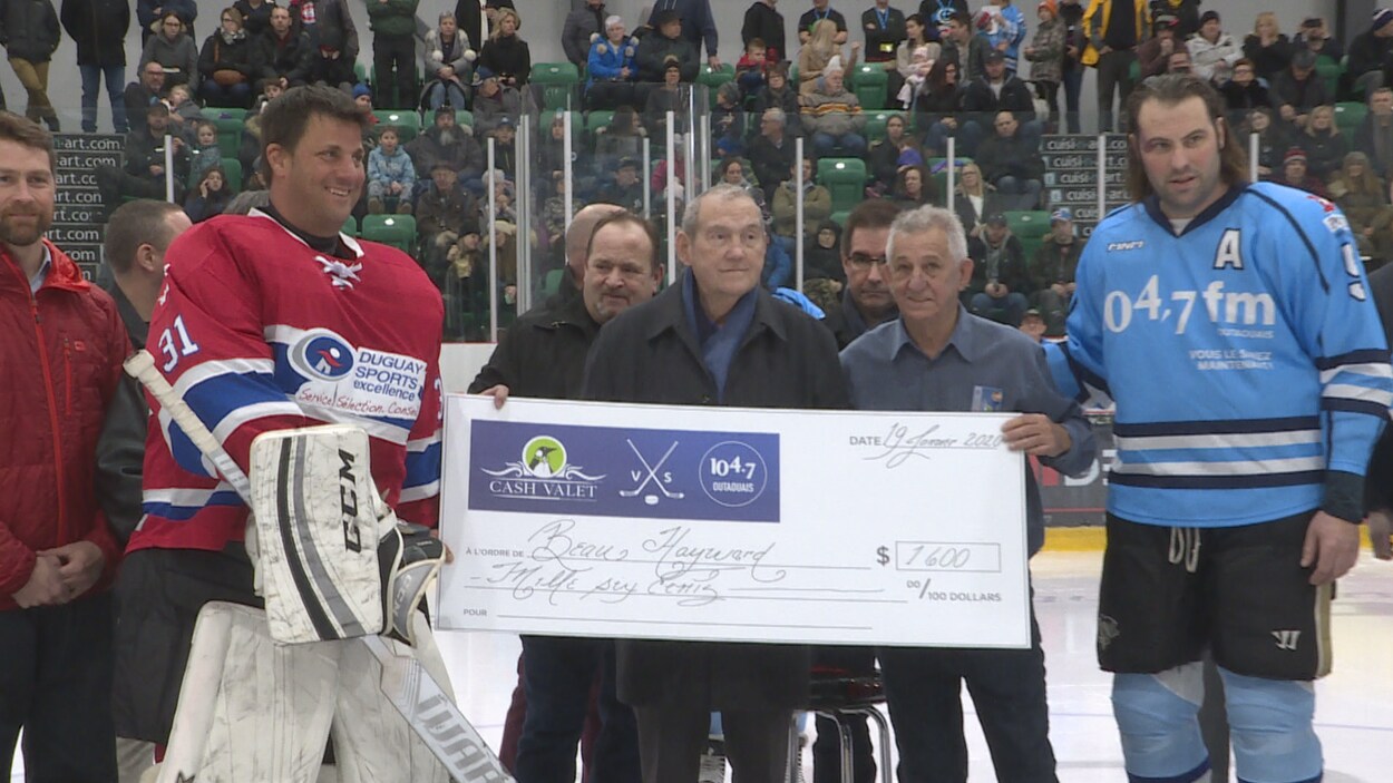 Deux joueurs de hockey tiennent un chèque gigantesque dans une arène.