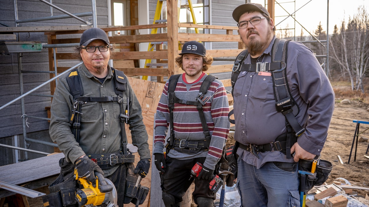 Une équipe de charpentiers prennent la pose devant une maison en construction.