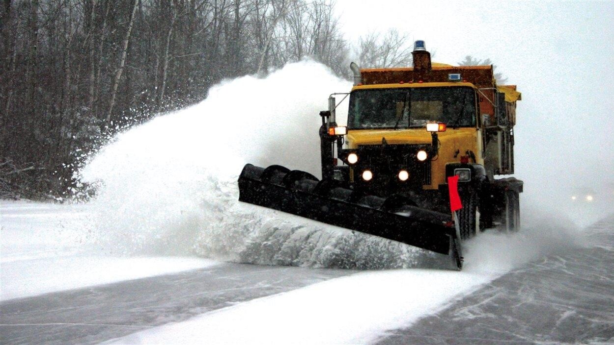Un chasse-neige sur une autoroute projette une gerbe de neige dans le fossé.