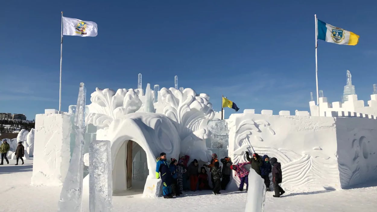 Sous un ciel bleu, des gens sont debout à côté du château de neige du Festival d'hiver Snowking.