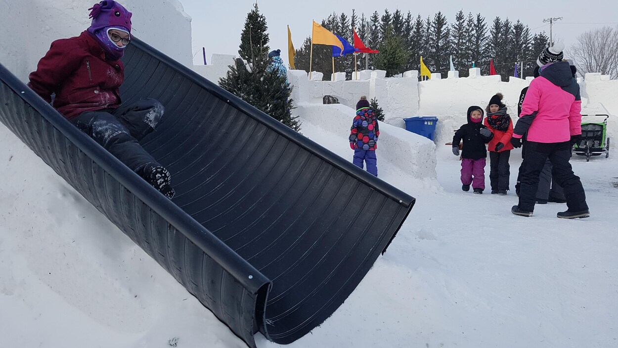 Une petite fille glisse dans un tuyau de plastique accroché à un château de neige.