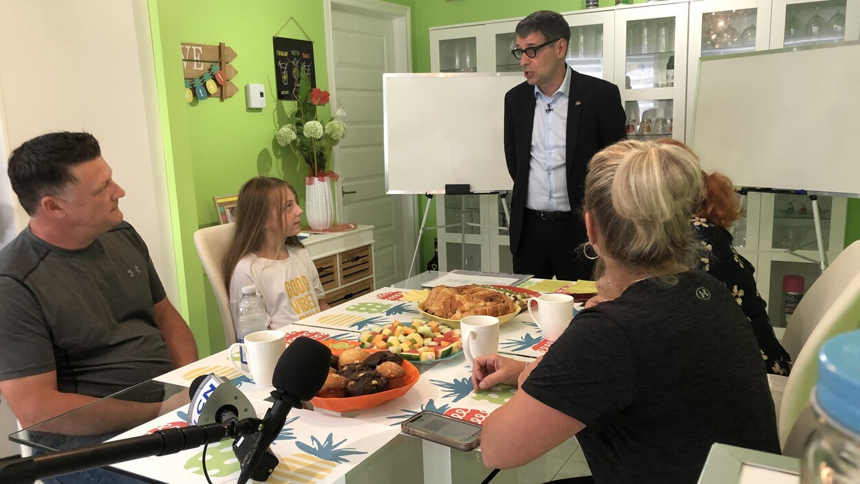 Éric Duhaime debout dans une cuisine, devant une famille assise à une table.