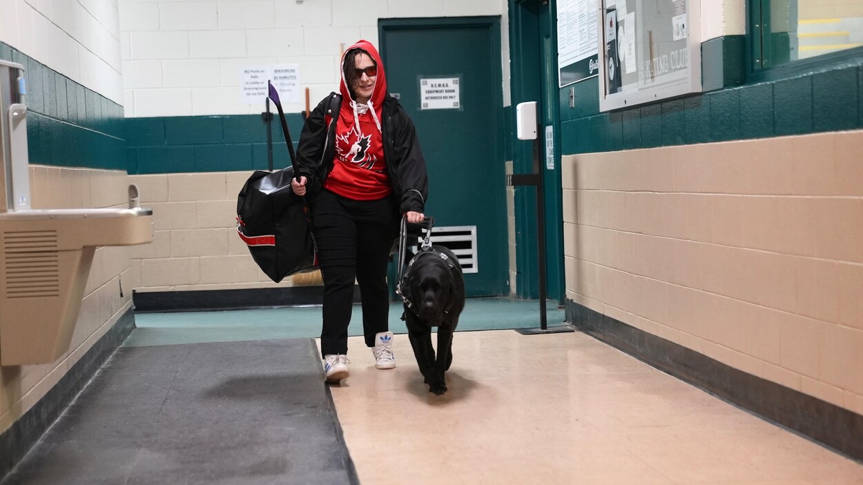 Une jeune femme marche dans un aréna avec son chien guide.