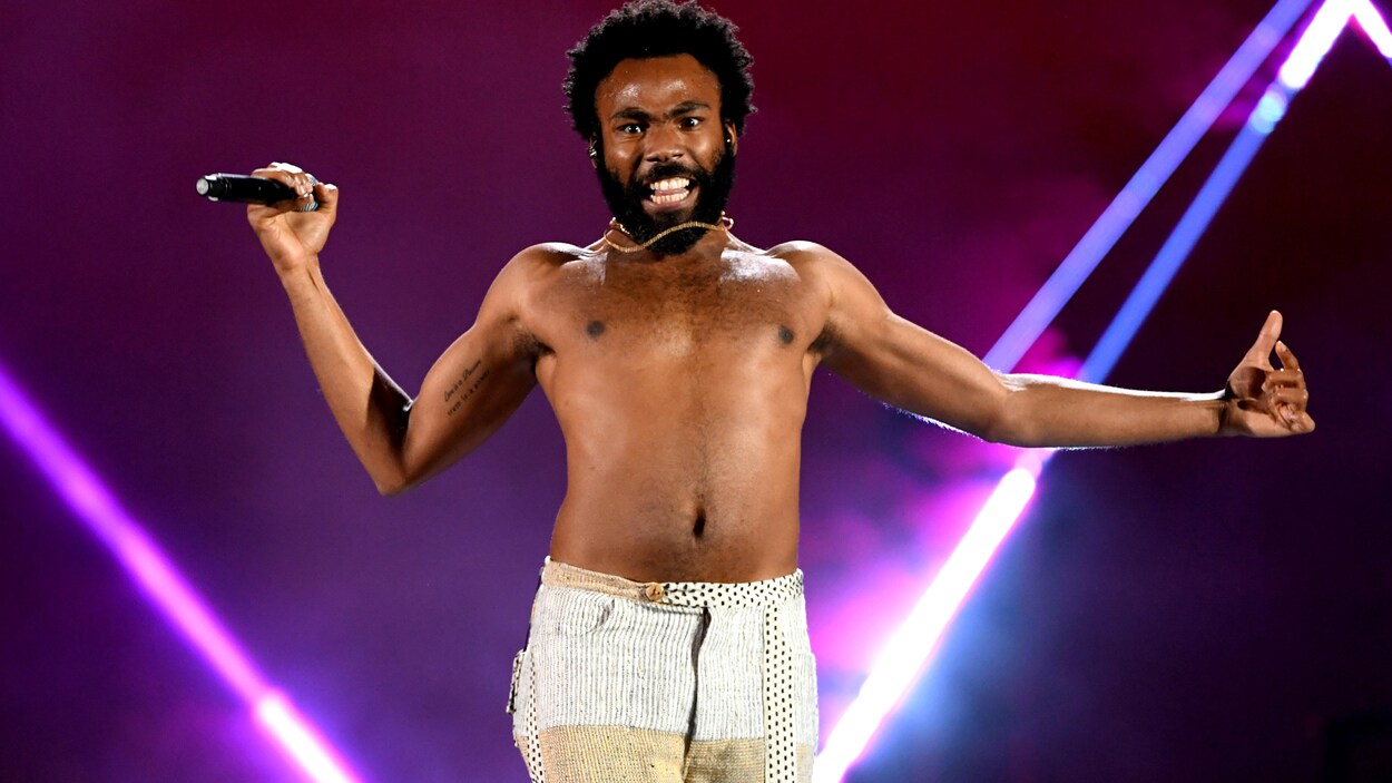 L'homme chante sur une scène avec un micro dans la main, torse nu.