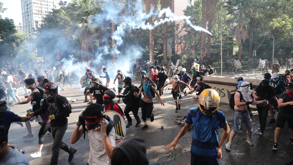 Des manifestants, portant des casques et des lunettes, poursuivis par des policiers.