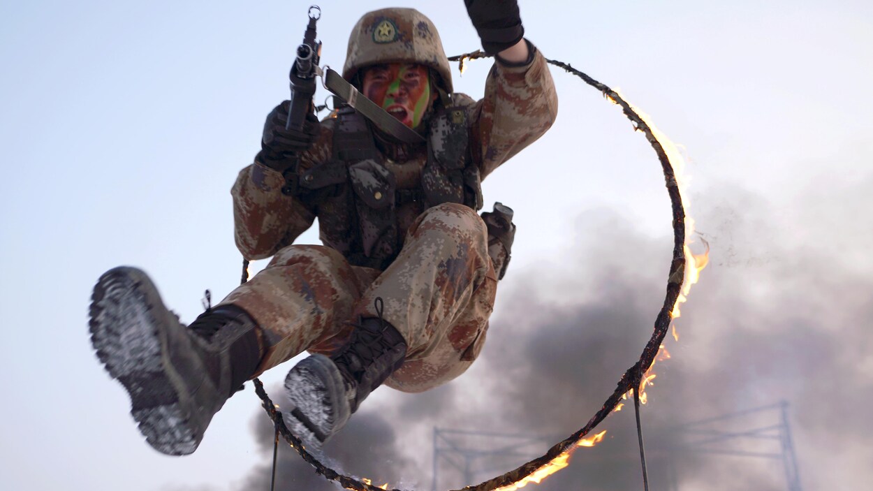 Un soldat chinois armé et en uniforme militaire saute dans un cerceau en feu.