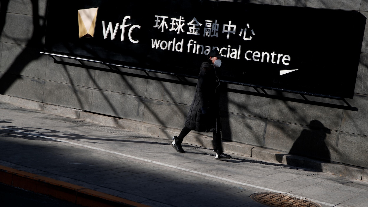 Une femme portant un masque passe devant un panneau indiquant World financial center.