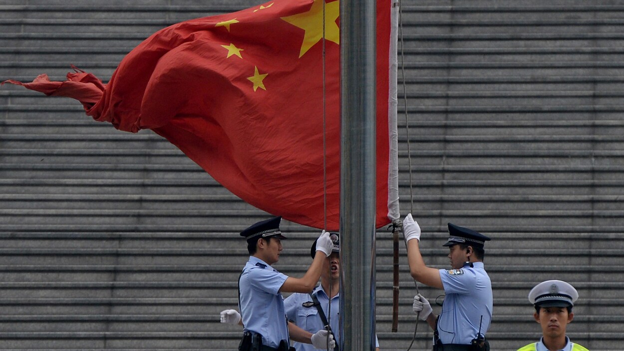 Trois policiers hissent le drapeau chinois devant un tribunal.