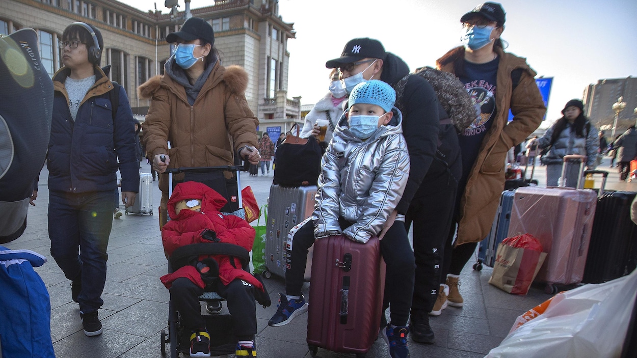 Plusieurs Chinois traînant des valises portent des masques à l'extérieur à Pékin.