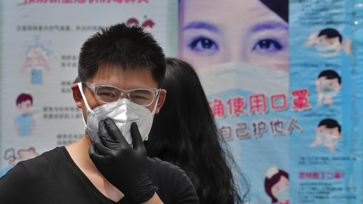 Un homme porte un masque de protection avec en arrière-plan des affiches expliquant la bonne façon de porter un masque facial pour aider à freiner la propagation du coronavirus à Pékin.