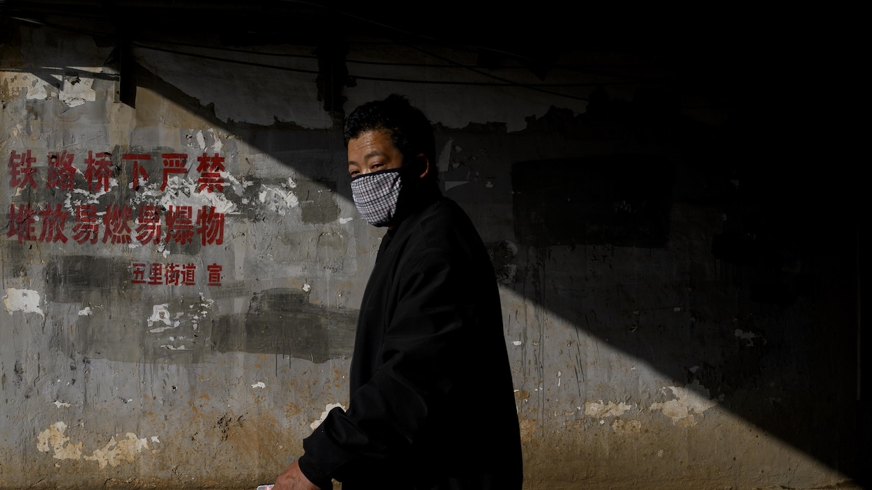 Un homme portant un masque sur la bouche marche dans la pénombre.