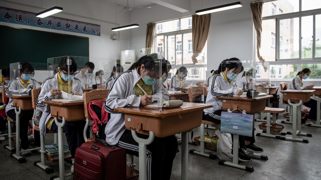 Des étudiants sont assis à des pupitres qui sont protégés par des panneaux de plexiglas.