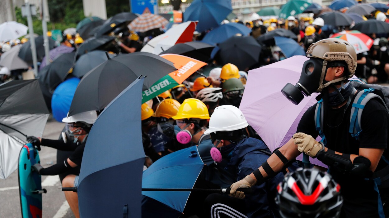 Des manifestants portant des masques se protègent avec des parapluies brandis devant eux.