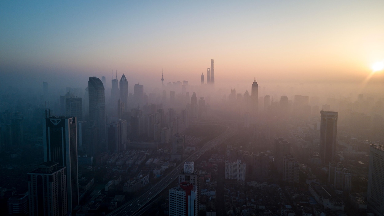 Une ville dont les bâtiments sont embrumés en raison de la pollution est vue de haut et de loin lors du lever du soleil.