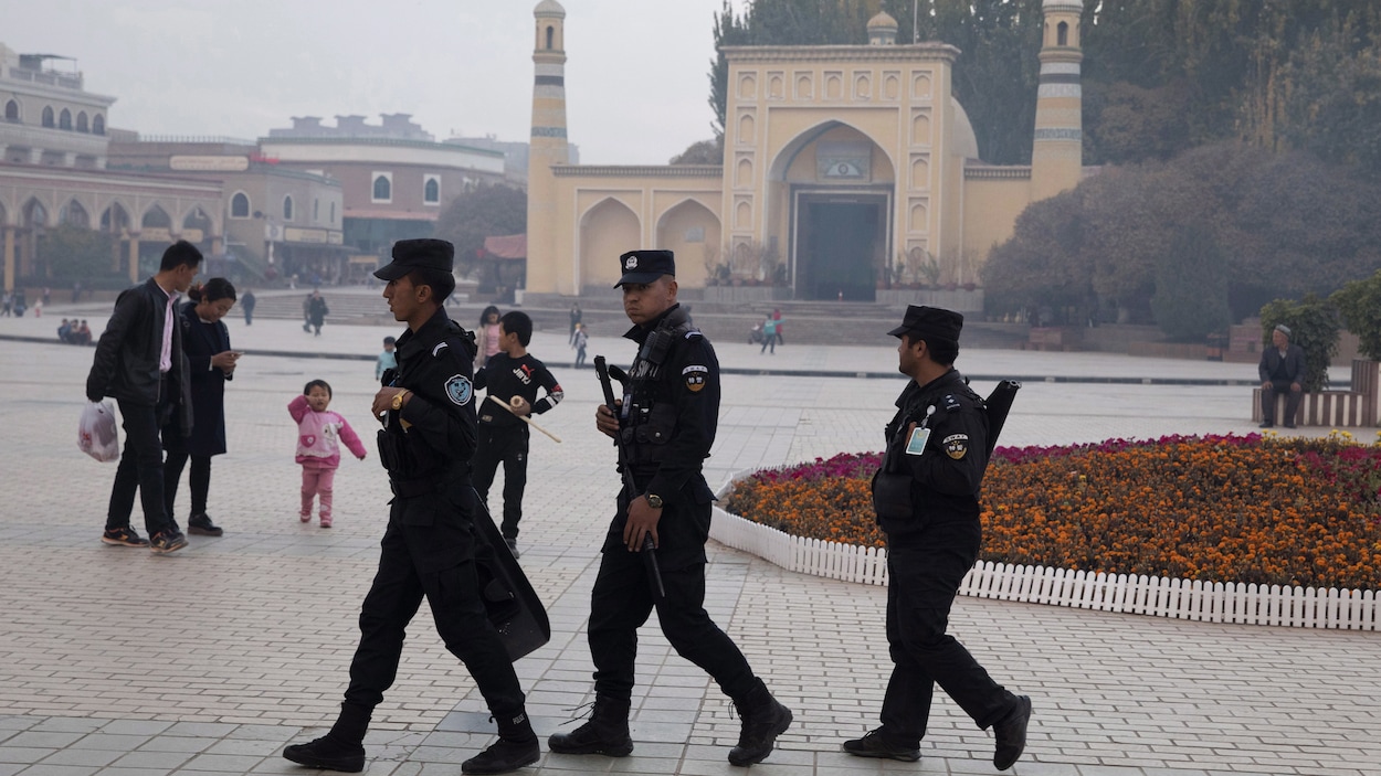 Trois agents de sécurité en uniforme marchent dans un espace public devant une mosquée.