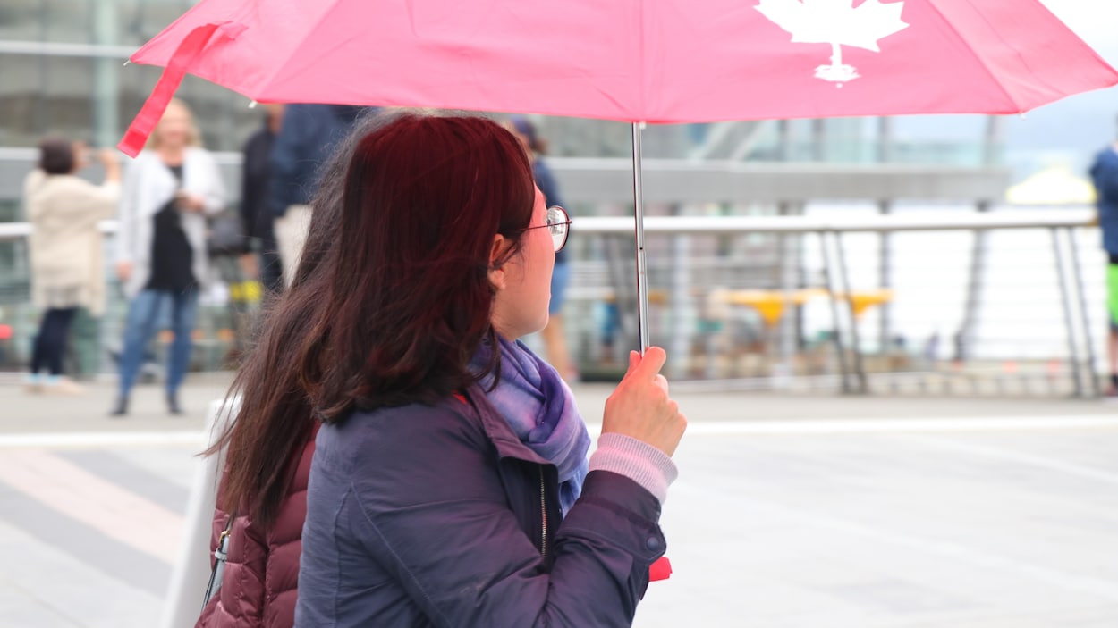 Une sino-canadienne sous un parapluie rouge arborant une feuille d'érable, à Vancouver.